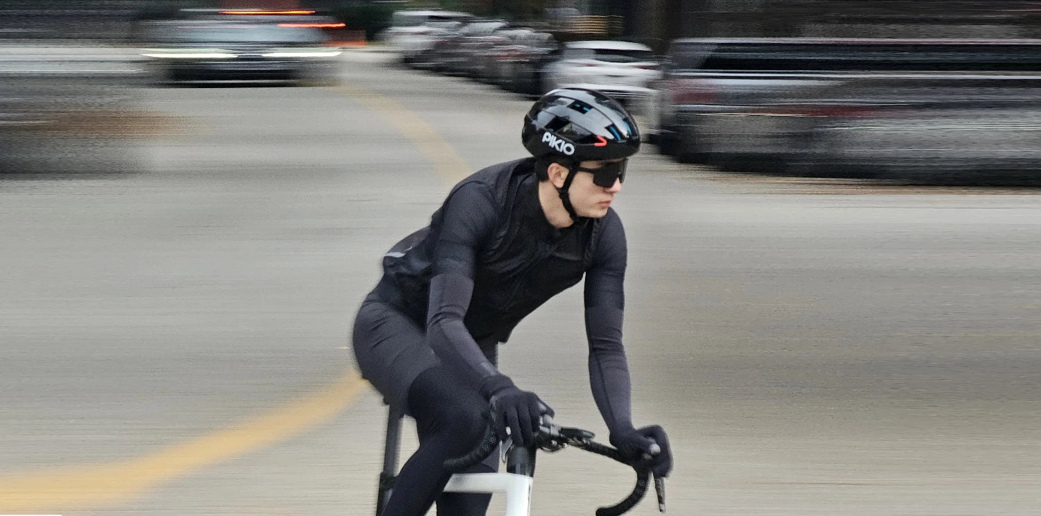 Cyclist riding down a city street with blurred background wearing a Black PIKIO helmet.
