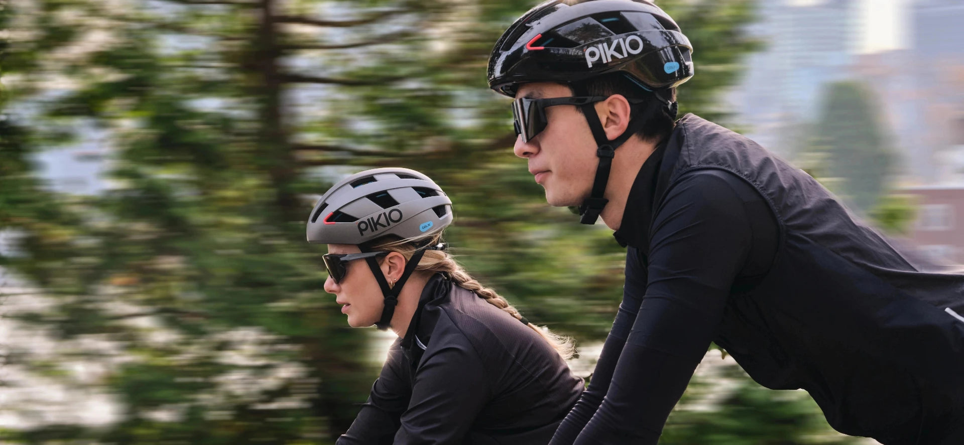 Two cyclists wearing PIKIO Si helmets riding outdoors.