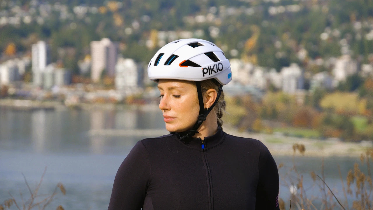 Person wearing a PIKIO Si helmet by a waterfront with a cityscape in the background